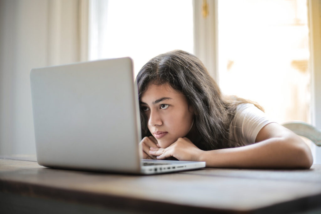 This is an image of a girl who's resting her head at a table with a laptop open in front of her. She appears bored. This is from an article about procrastination and productivity that says that boredom is one of the reasons why we procrastinate and discusses some strategies to beat that