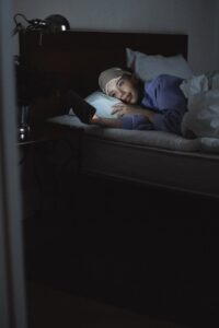 woman lying on bed while using a cellphone
